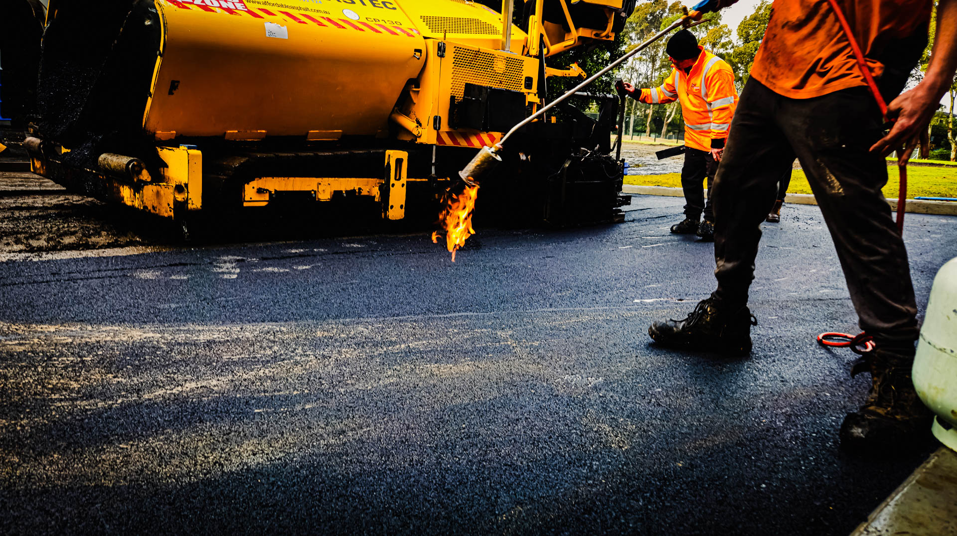 Man holding flame torch for road sealing with yellow asphalt truck and asphalt road